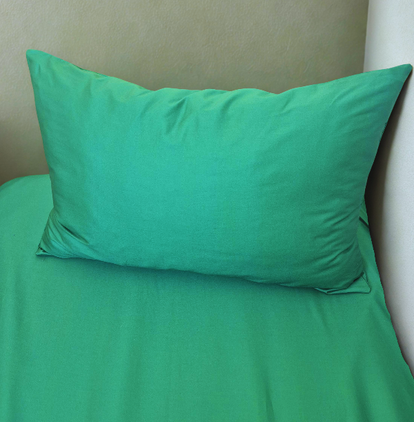 Green pillow and sheet set on a bed against a beige wall.