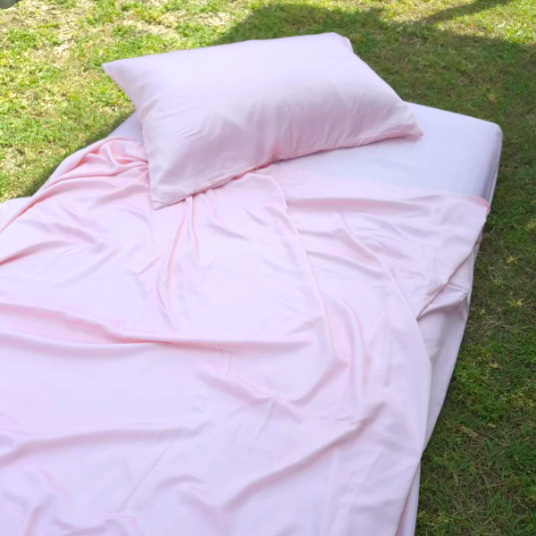 Pink bedding set on a bed outdoors with grass in the background