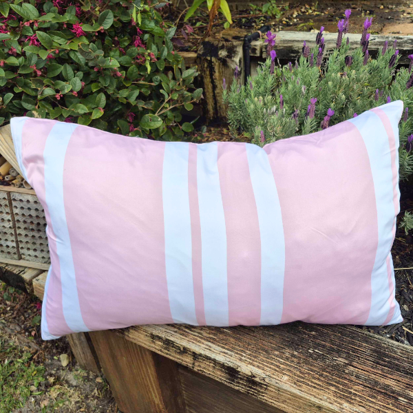 Pink and white striped pillow on a wooden bench with plants in the background