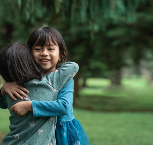 Two children hugging outdoors with a blurred green background