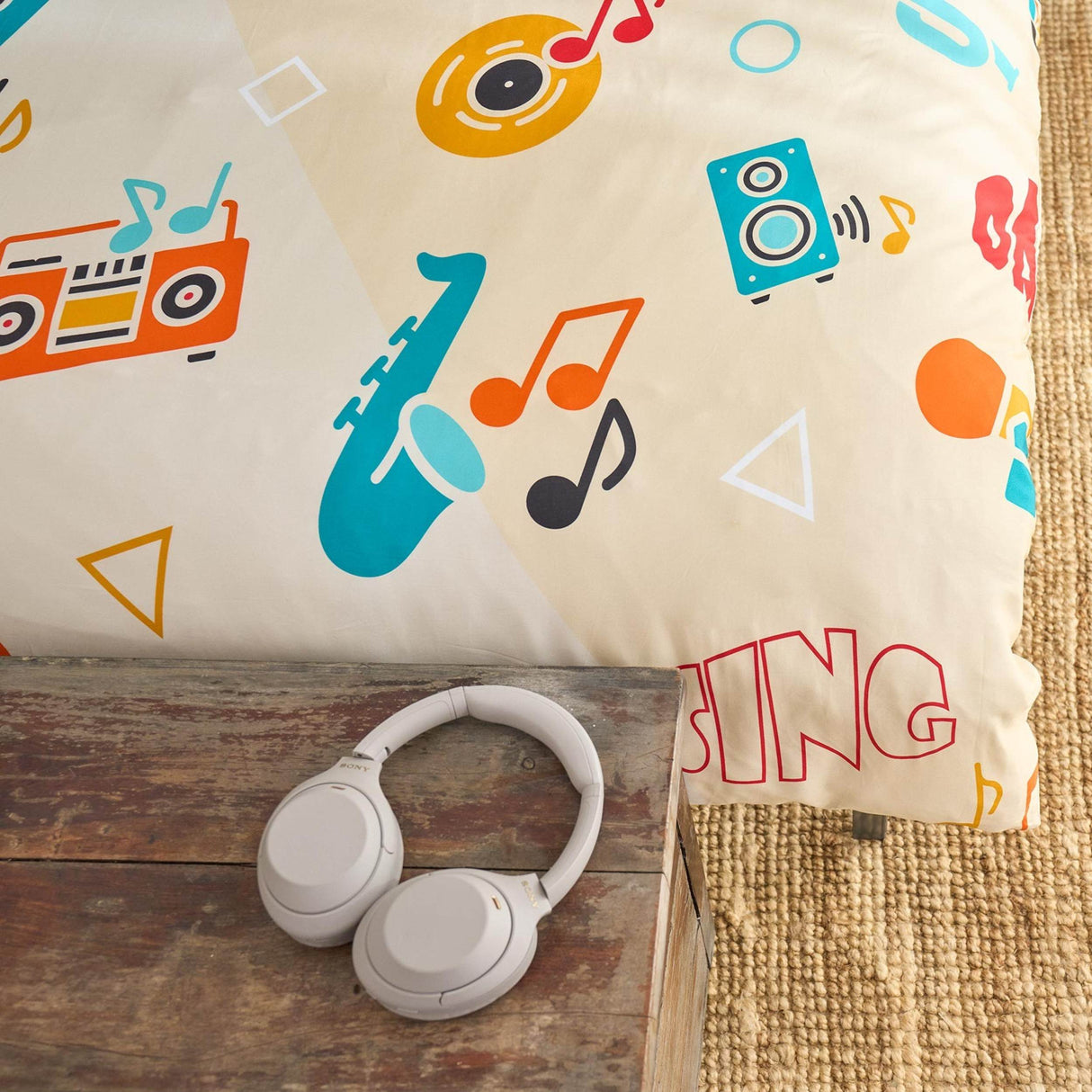 Music-themed quilt cover with colorful designs and 'SING' text, next to a pair of white headphones on a wooden surface.