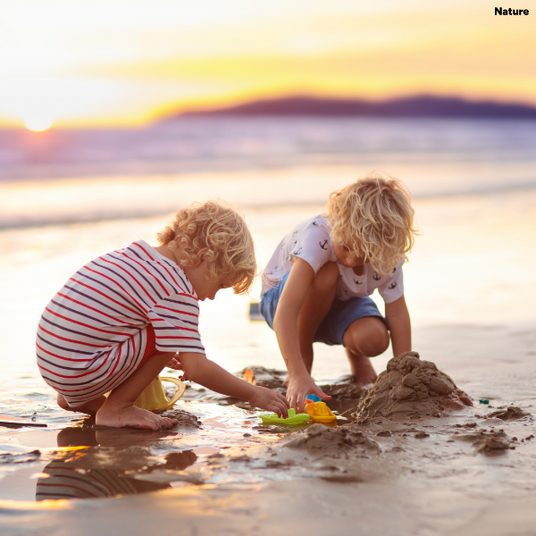 Two children playing in the sand on a beach at sunset.
