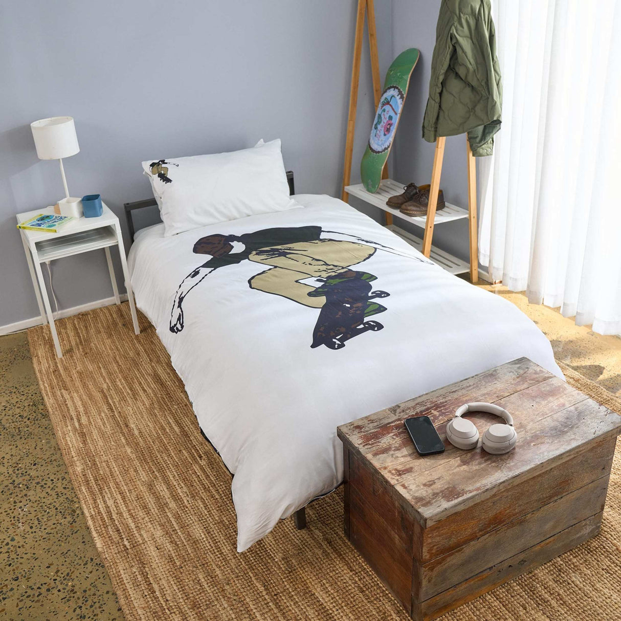 Bedroom with a bed featuring a skateboarder, wooden nightstand, and skateboard on a shelf.