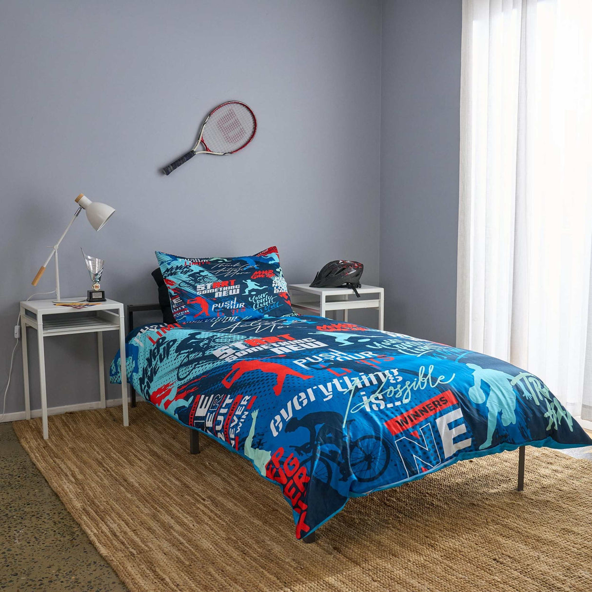 Bedroom with 'Sports Motivation' themed bedding set, tennis racket on wall, and small table with lamp.