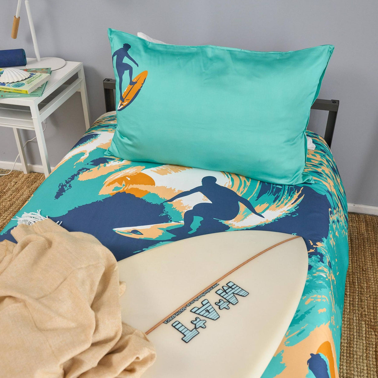 Bedding set with surf design and teal pillow on a bed