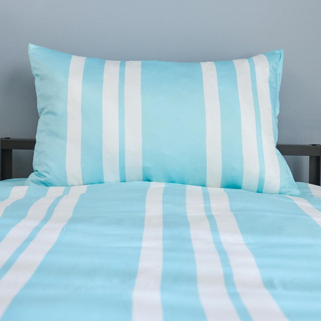 Striped blue and white bedding set on a bed with a gray wall background