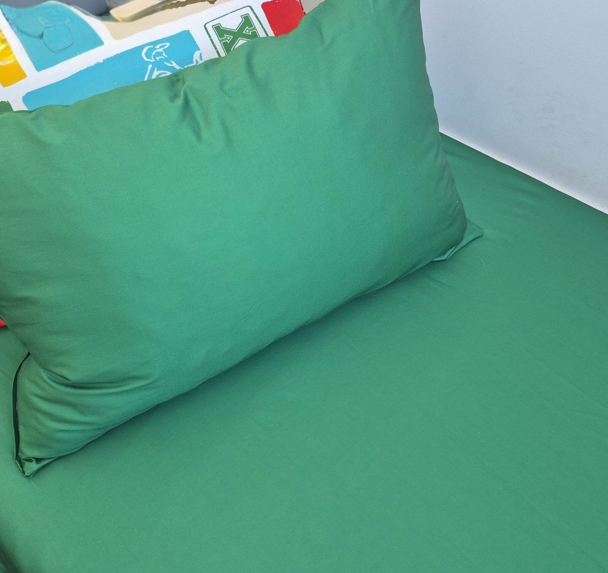 Green pillow on a green bedspread with colorful pillow in the background