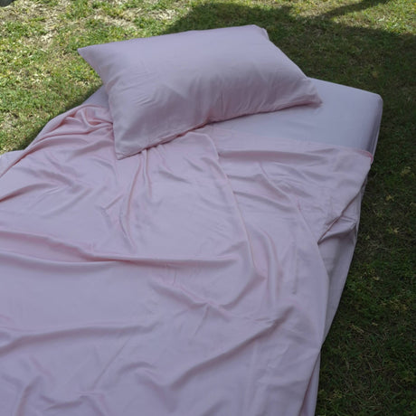 Pink sheets and pillow on a grassy surface