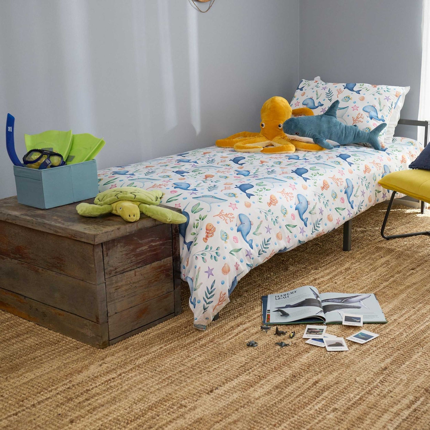 Children's bedroom with a bed featuring a colorful bedding set, toys, and books on a wooden bench.