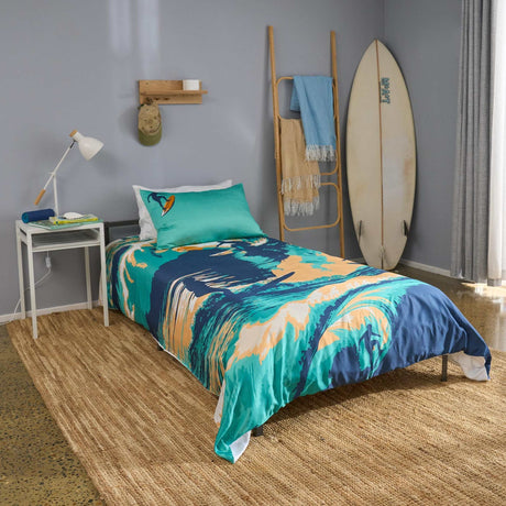 Bedroom with a bed featuring a colourful surfing themed quilt cover, a surfboard against the wall, and a nightstand with a lamp.