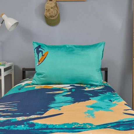 Teal pillowcase with a surf design on a bed with matching bedding in a room.